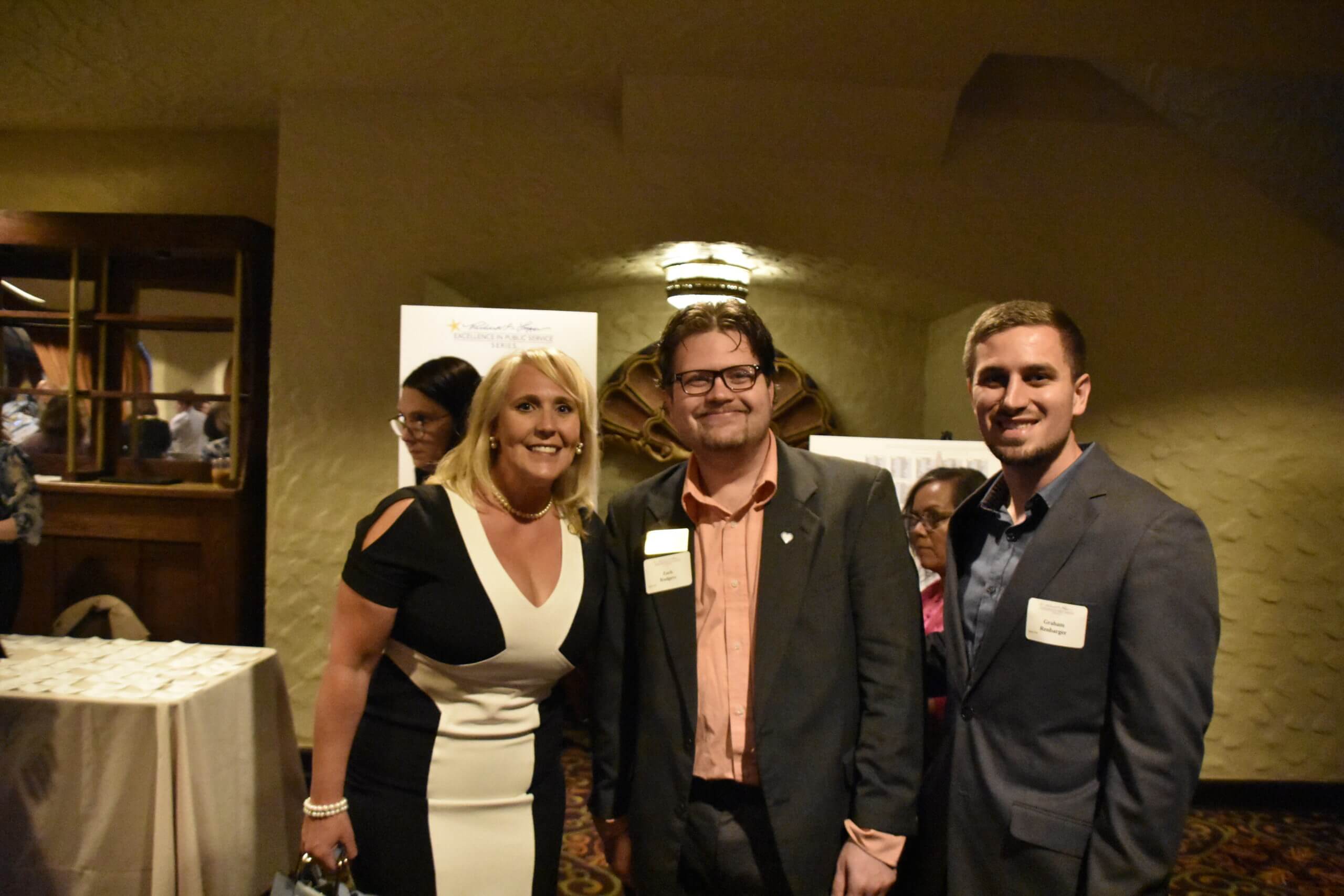 Event attendees smile for the camera – the woman is wearing a black and white dress