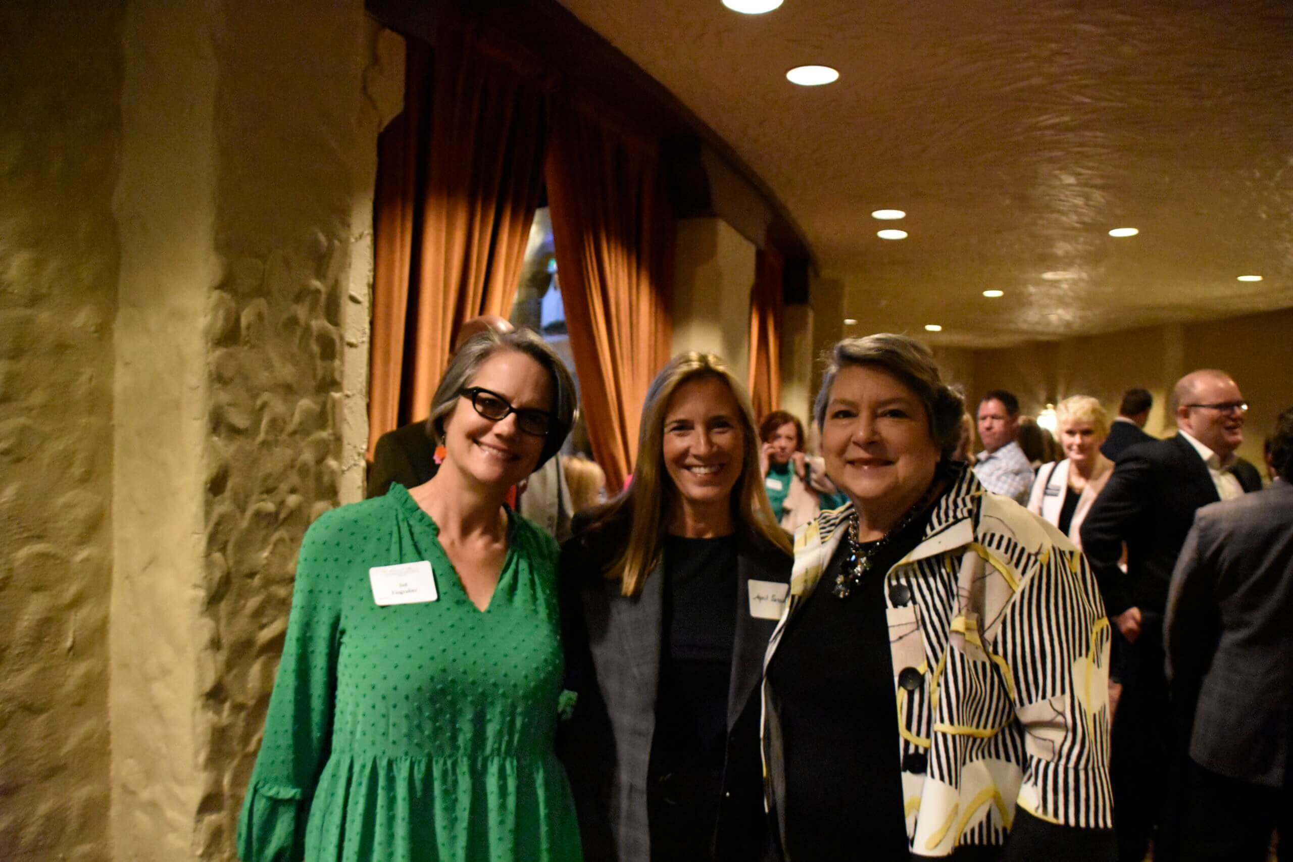 Three event attendees smile — one of the women is wearing a green shirt