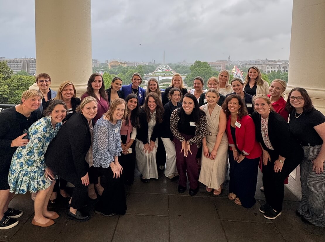 Members of the Lugar Series smile on a Capitol Hill balcony, overlooking the National Mall