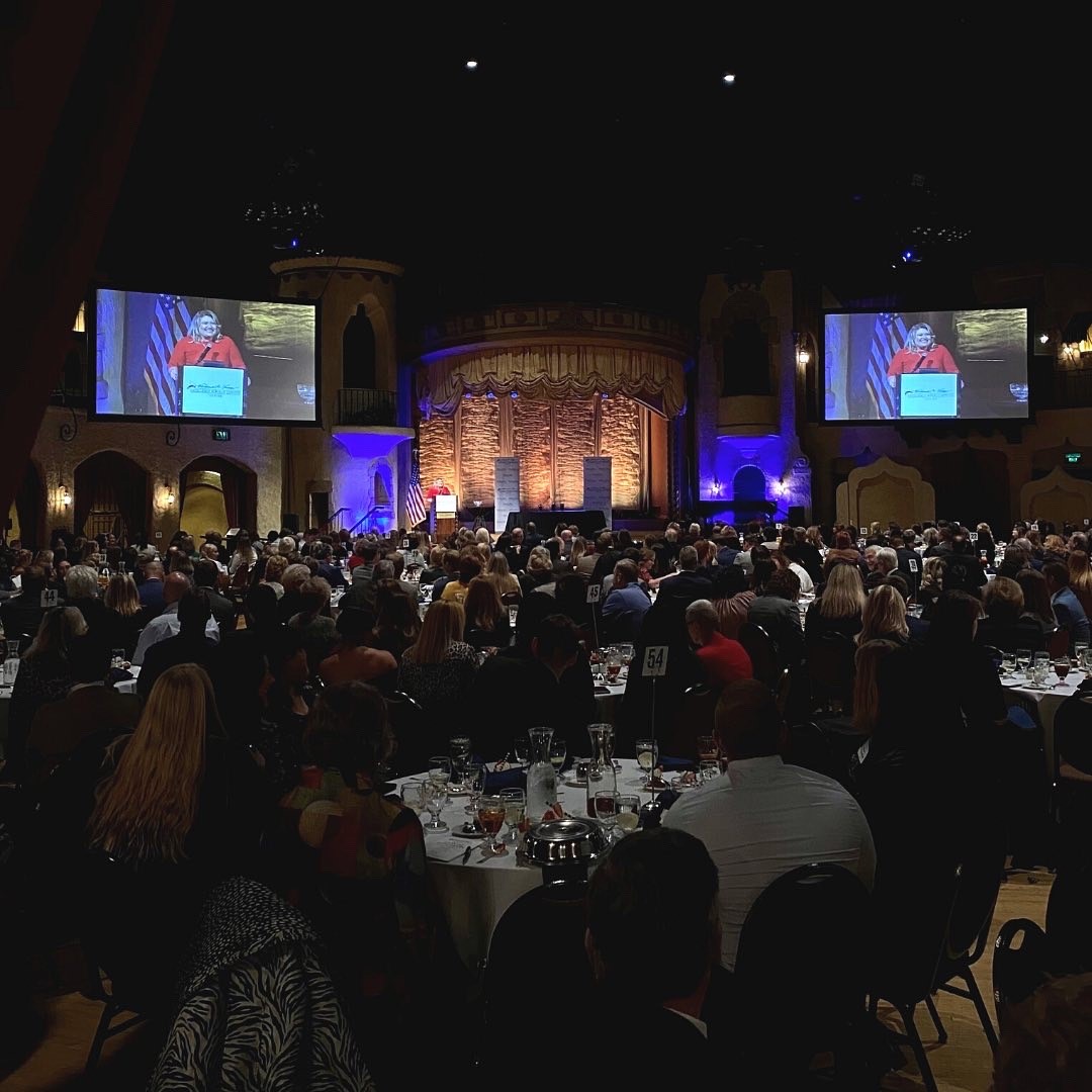 Attendees at tables watch blonde woman speak at Lugar Series 2021 Event